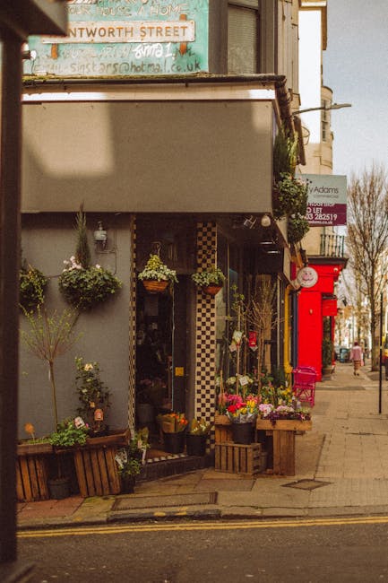 An outdoor display of potted plants and flowers arranged along the storefront of a garden center on Putney High Street. The displays include various flowering plants, leafy herbs, and green foliage in